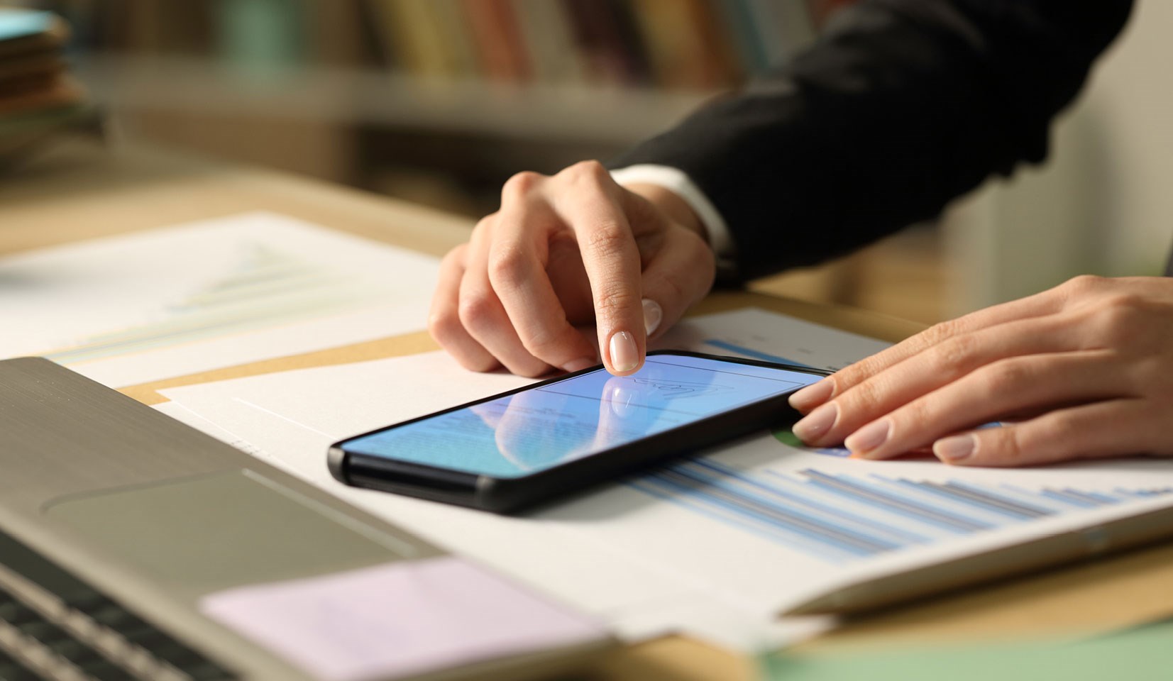 hand using a smartphone that is resting on a desk